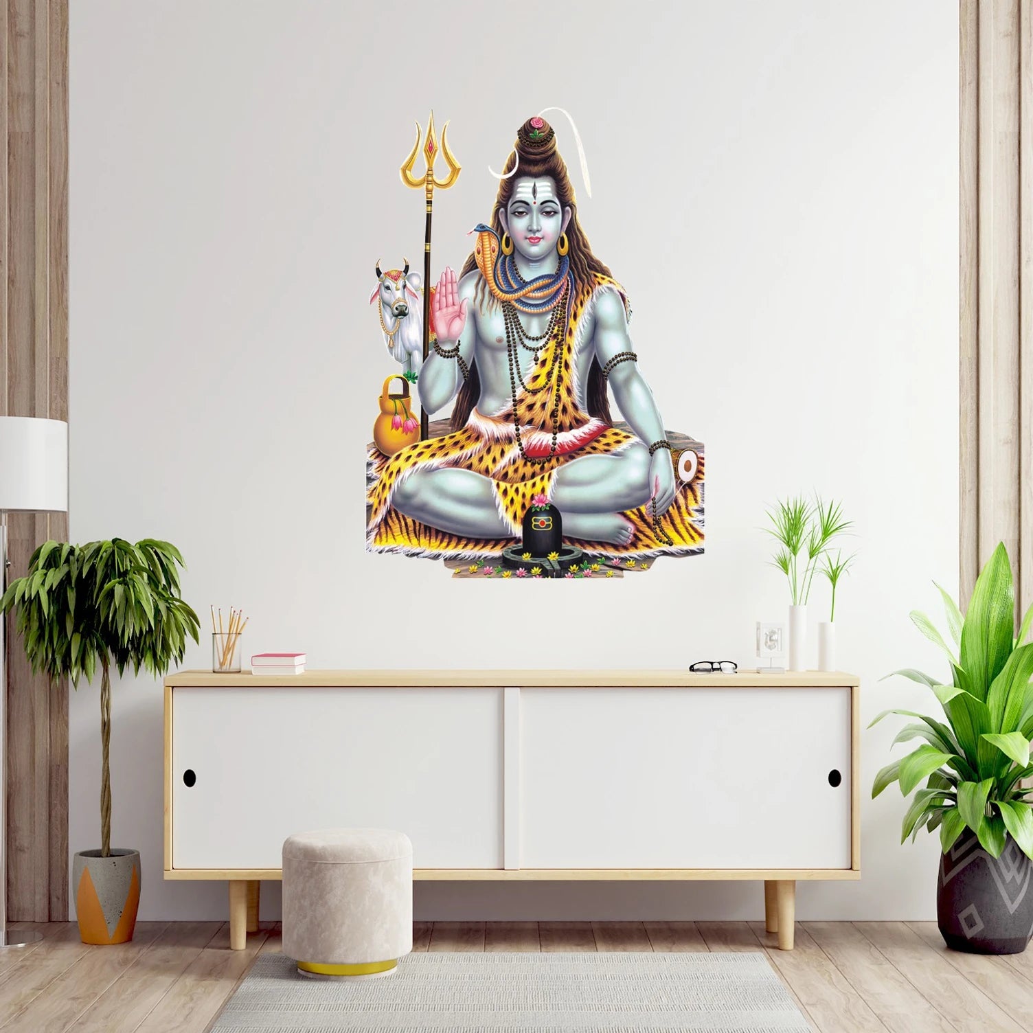 Wall art of a seated Shiva with a trident on a white wall above a white cabinet.