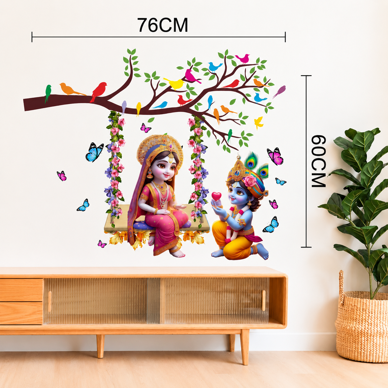 Wall decal of Radha Krishna on a swing with tree and birds, placed above a wooden cabinet.