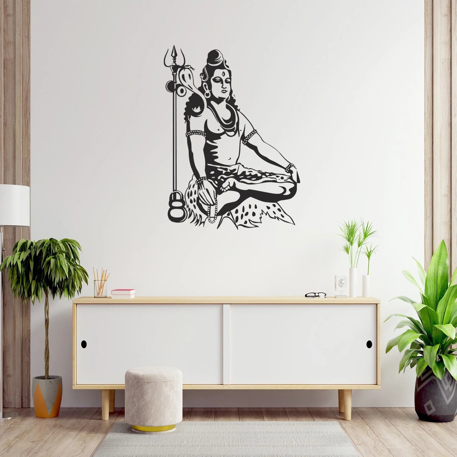 Wall decal of a seated Shiva with a trident on a white wall above a wooden cabinet.